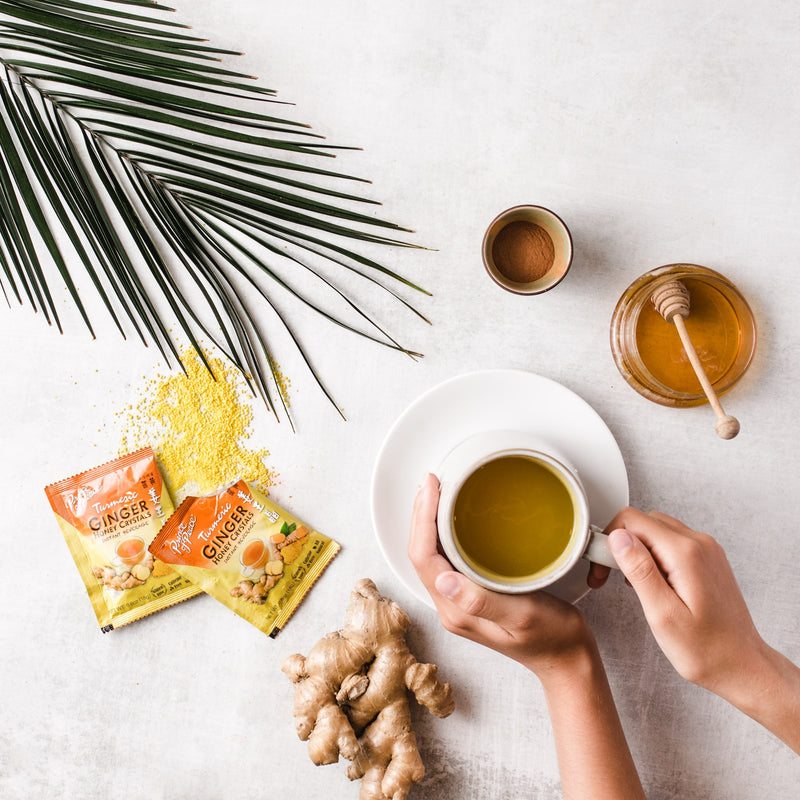 A cup of Prince of Peace Instant Ginger Honey Crystals Turmeric with opened sachet and ginger on a table.