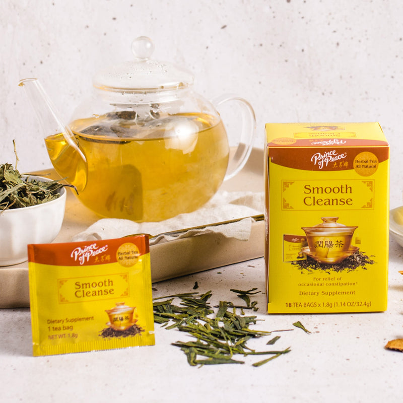 A package of Prince of Peace Smooth Cleanse Tea, a sachet and the ingredients in front of a glass teapot.